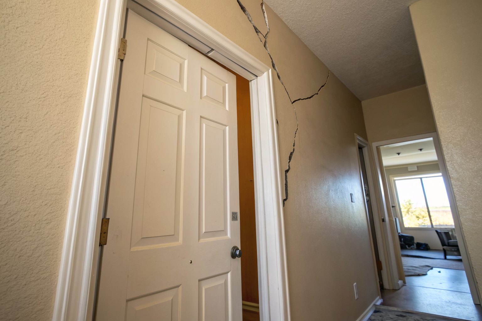 Interior door with a wedge-shaped gap at the top and a wall crack above it