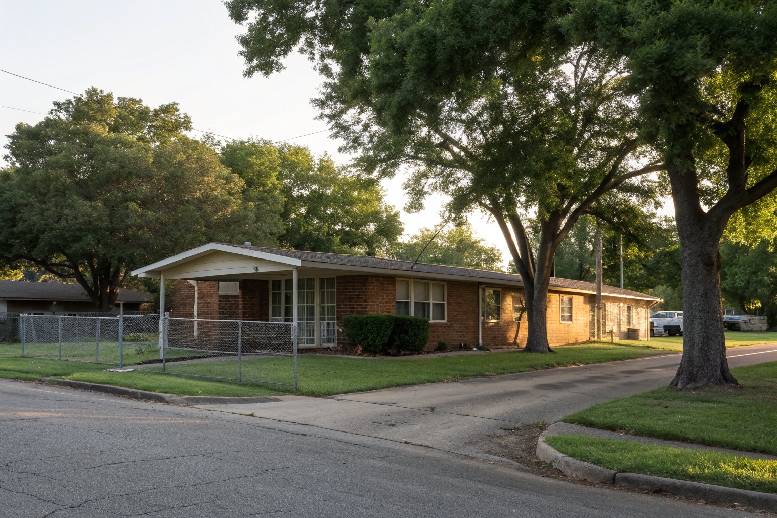 1960s brick house with a carport and a chain-link fence